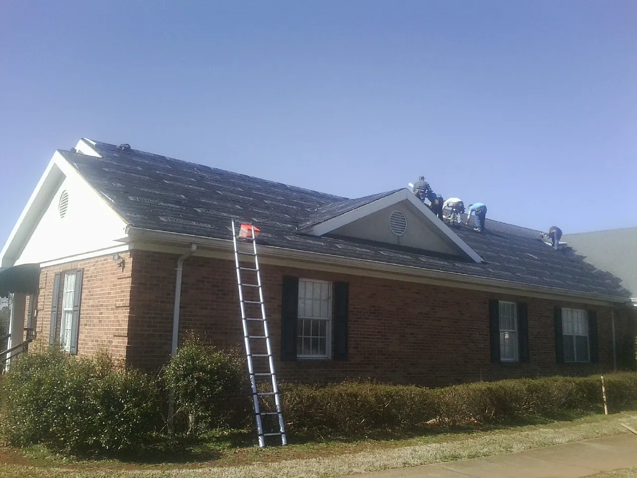 Crew tearing shingles off a brick ranch roof with a ladder set — Metal Roof Repair work by our crew in Miamitown