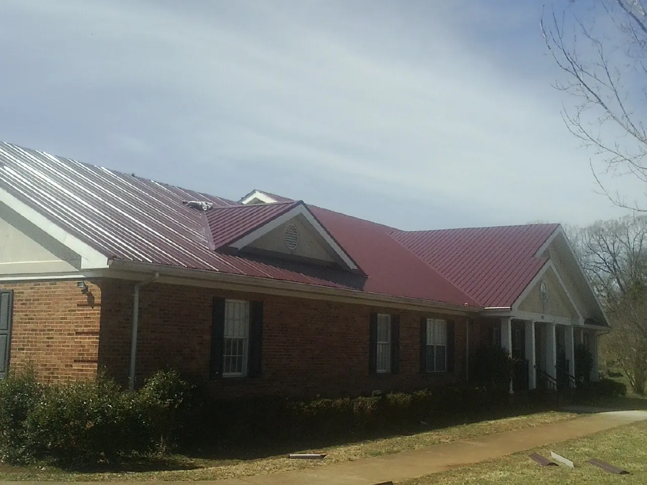 Red metal roof with gabled entries on a long brick building, from a Hail Damage Roof Repair job in Miamitown