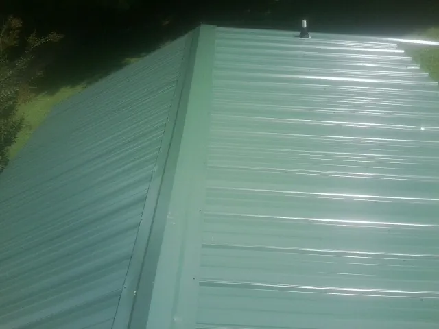 New green metal panels meeting at the ridge of a roof — Flat Roof Repair work by our crew in Miamitown