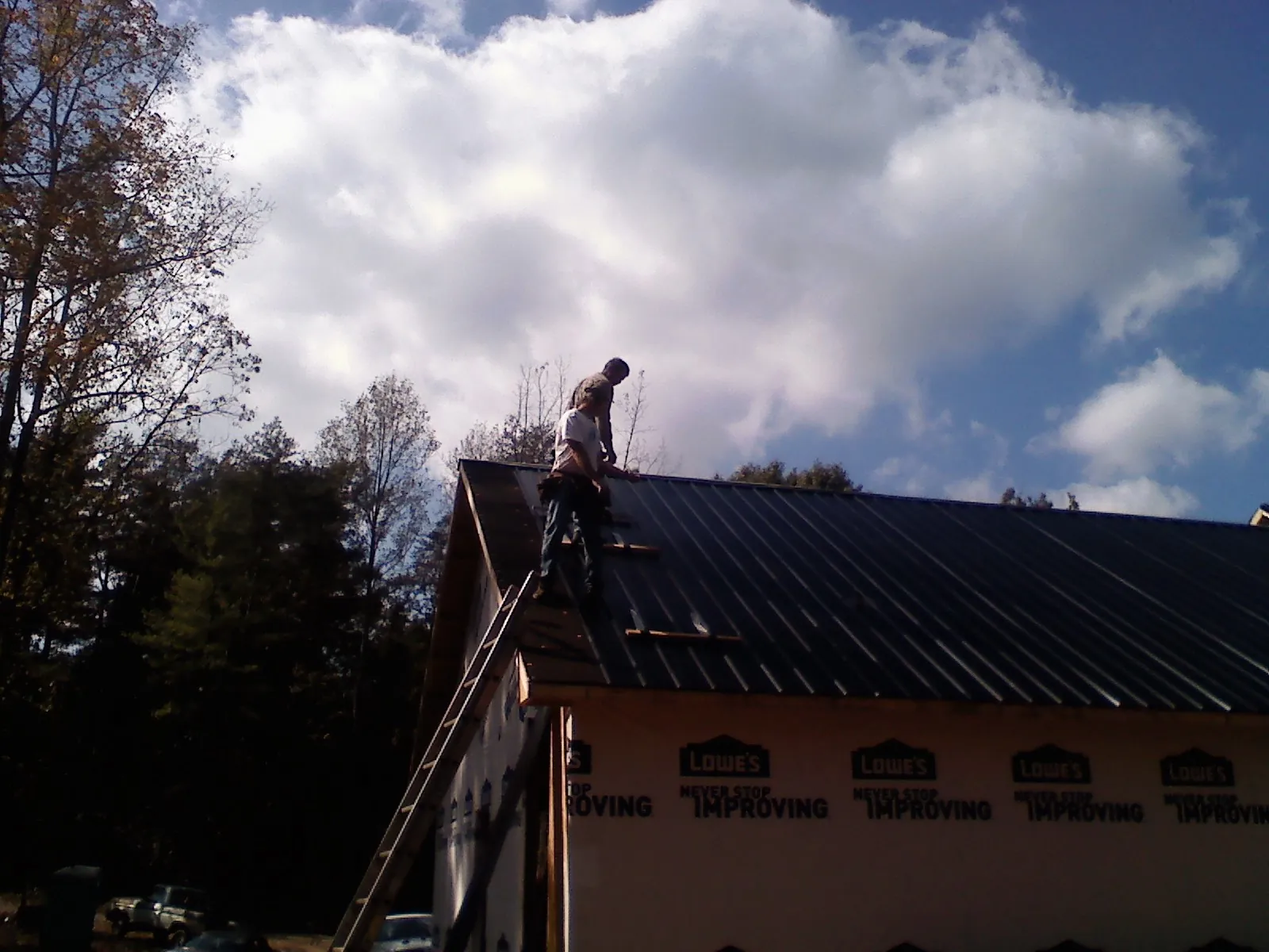 Roofer fastening dark metal panels high against a cloudy sky, from a Roof Inspection job in Miamitown