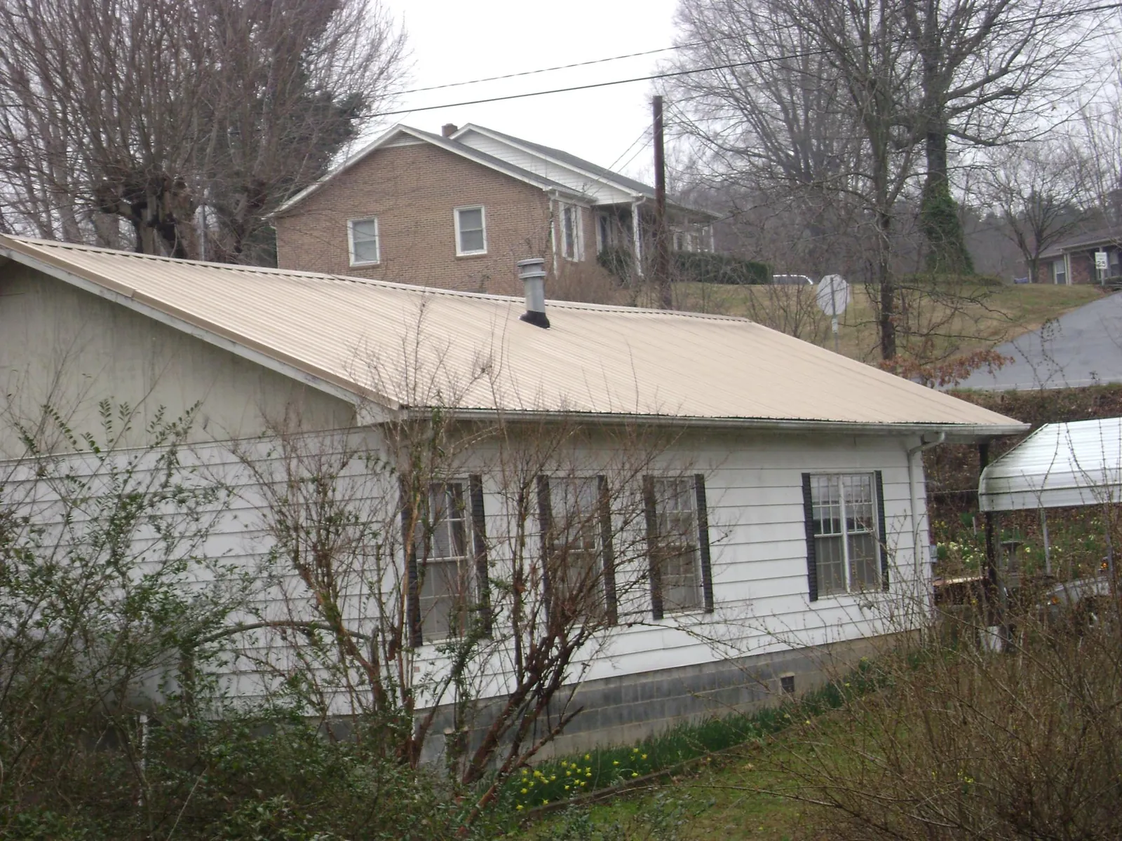 Tan metal roof on a white sided house set into a hillside — Commercial Roofing by Roofing Brothers in Miamitown